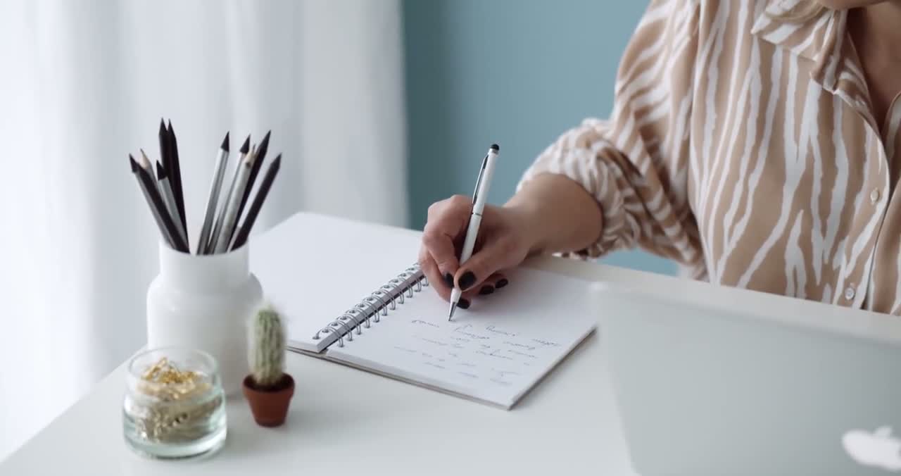 Woman writing notes beside her laptop